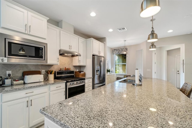 kitchen with appliances with stainless steel finishes, pendant lighting, backsplash, a center island with sink, and white cabinets