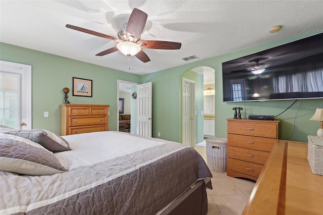 tiled bedroom with ensuite bath, ceiling fan, and a textured ceiling