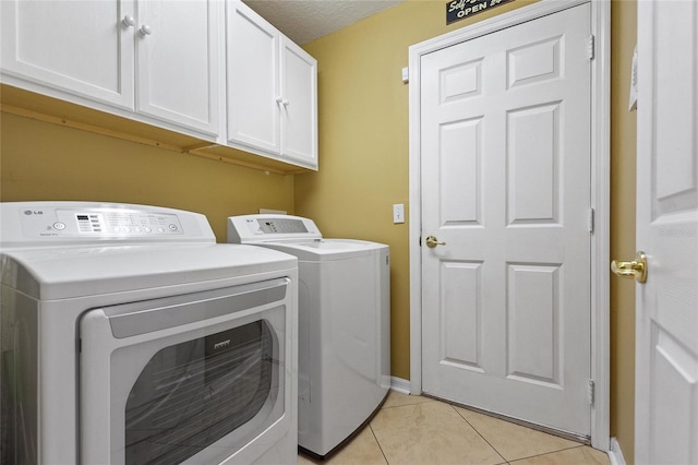 clothes washing area featuring a textured ceiling, cabinets, separate washer and dryer, and light tile floors