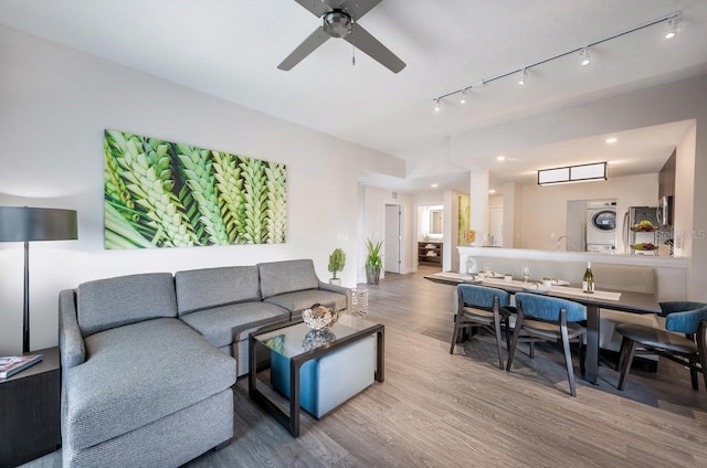 living room featuring rail lighting, stacked washer and clothes dryer, ceiling fan, and hardwood / wood-style floors