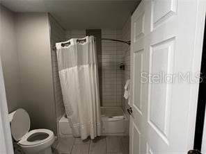 bathroom with toilet, shower / tub combo, and tile patterned floors