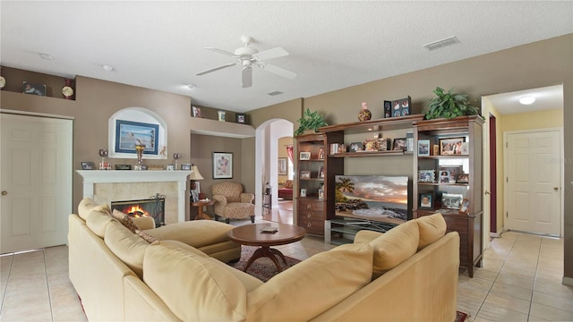 tiled living room with ceiling fan, a textured ceiling, and a fireplace