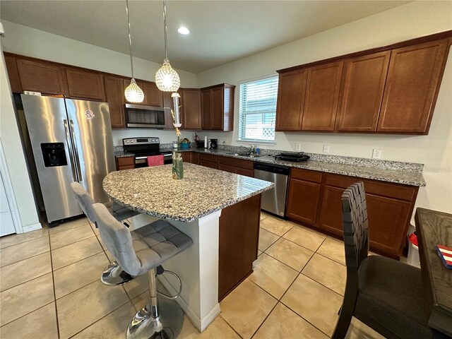 kitchen with appliances with stainless steel finishes, a kitchen breakfast bar, light stone counters, decorative light fixtures, and a kitchen island