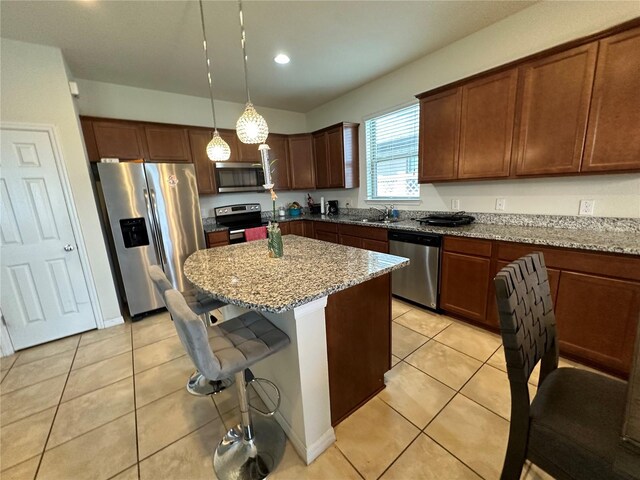 kitchen with a center island, light stone counters, decorative light fixtures, light tile patterned floors, and appliances with stainless steel finishes