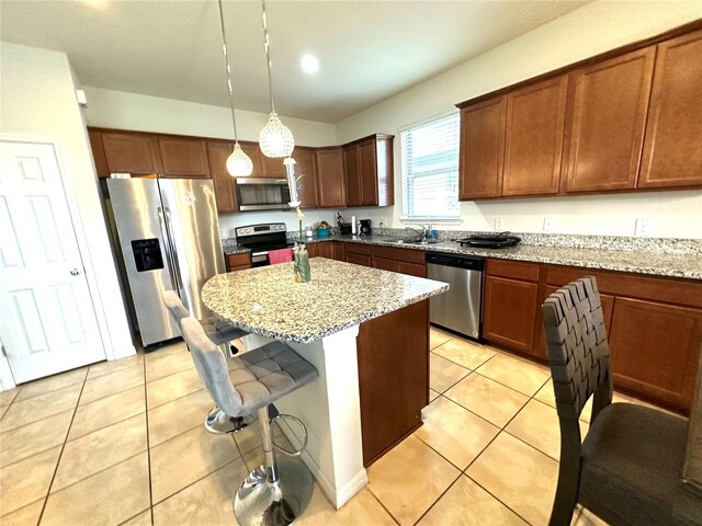 kitchen with light tile patterned floors, stainless steel appliances, light stone counters, and hanging light fixtures