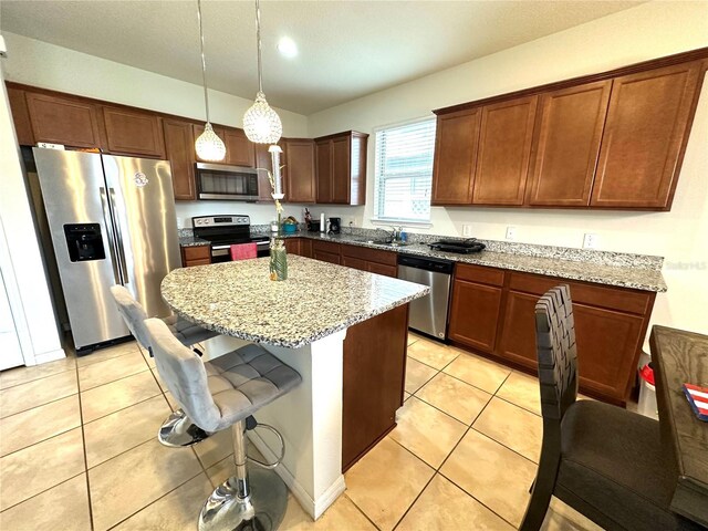 kitchen with light stone countertops, hanging light fixtures, a breakfast bar, light tile patterned flooring, and appliances with stainless steel finishes