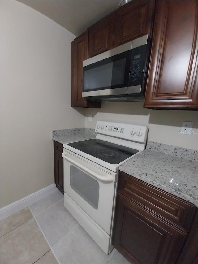 kitchen featuring white range with electric cooktop, light tile patterned flooring, dark brown cabinetry, and light stone countertops