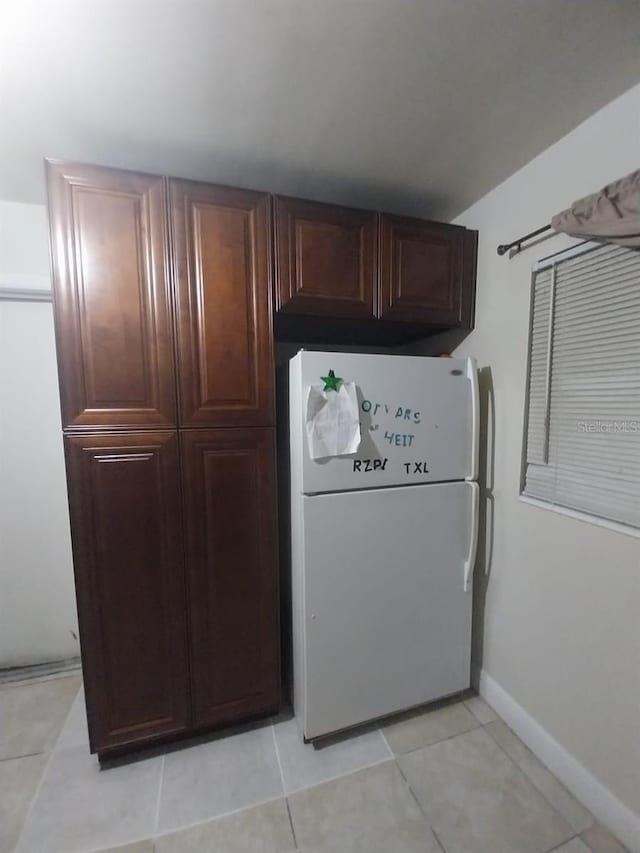 kitchen with dark brown cabinets, white fridge, and light tile patterned flooring