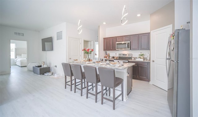 kitchen with a breakfast bar area, light hardwood / wood-style flooring, light stone countertops, an island with sink, and stainless steel appliances