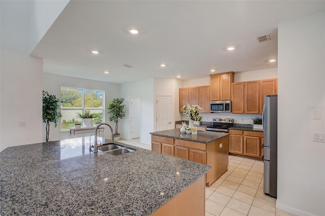 kitchen with appliances with stainless steel finishes, dark stone counters, sink, a kitchen island with sink, and light tile patterned flooring