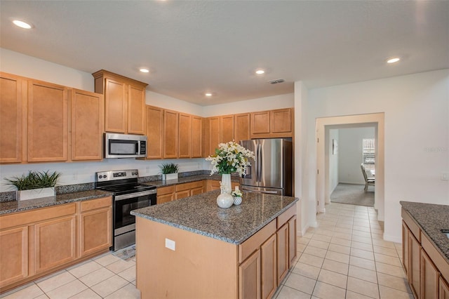 kitchen featuring appliances with stainless steel finishes, dark stone countertops, light colored carpet, and a kitchen island