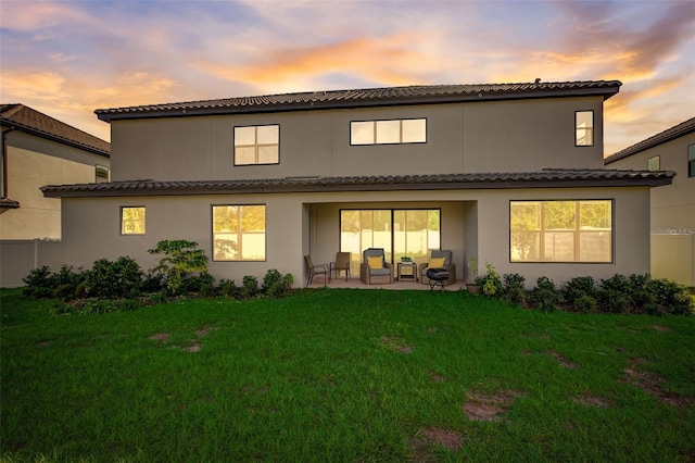 back house at dusk featuring a patio and a lawn