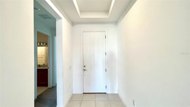 hallway with light tile patterned floors, sink, and a tray ceiling