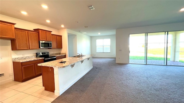 kitchen featuring a kitchen bar, sink, appliances with stainless steel finishes, an island with sink, and light carpet