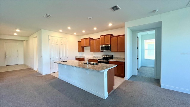 kitchen featuring appliances with stainless steel finishes, light carpet, sink, light stone counters, and a center island with sink