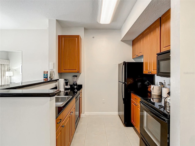 kitchen with light tile patterned floors, baseboards, black appliances, brown cabinetry, and dark countertops