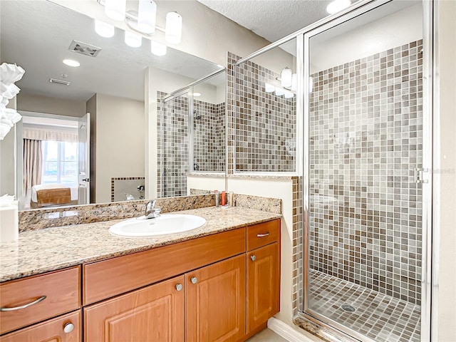 ensuite bathroom with visible vents, connected bathroom, a textured ceiling, vanity, and a shower stall