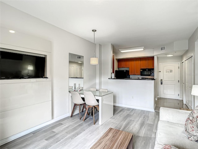 kitchen with visible vents, light wood-style floors, dark countertops, fridge, and black microwave