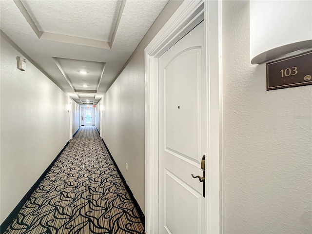 corridor with carpet floors, a textured ceiling, and a textured wall