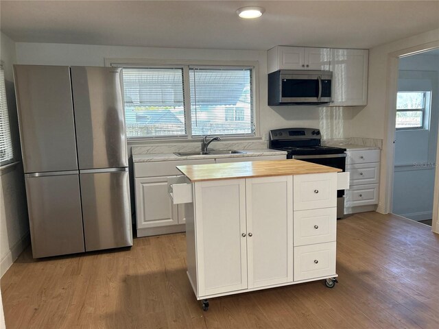 kitchen with appliances with stainless steel finishes, light hardwood / wood-style floors, white cabinetry, and sink