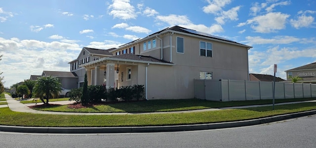 view of side of home featuring a yard, solar panels, stucco siding, and fence