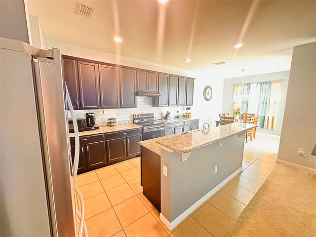 kitchen with a kitchen bar, appliances with stainless steel finishes, light tile patterned floors, decorative backsplash, and light stone countertops