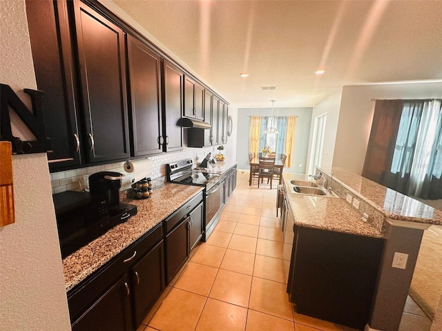 kitchen with an island with sink, light tile patterned flooring, a sink, stainless steel range with electric stovetop, and backsplash