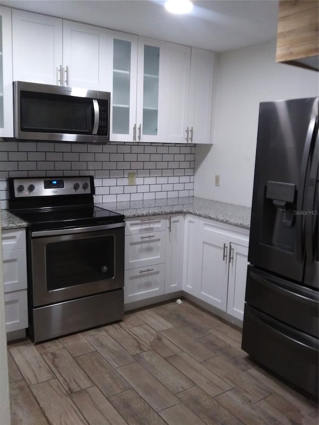 kitchen featuring light stone countertops, backsplash, light hardwood / wood-style flooring, stainless steel appliances, and white cabinets