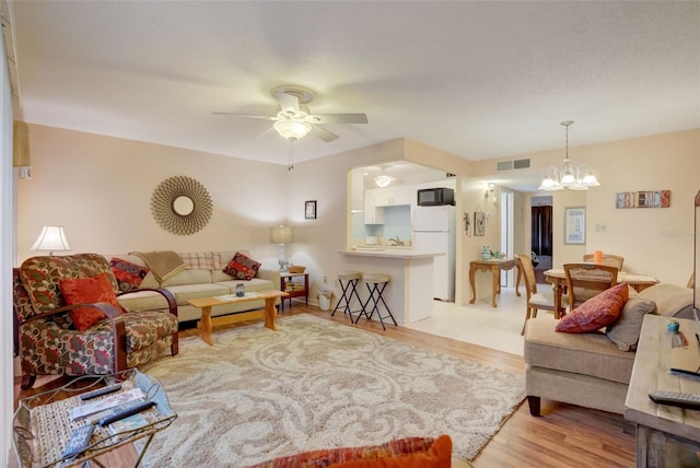 living room with ceiling fan with notable chandelier, light wood-type flooring, and a textured ceiling