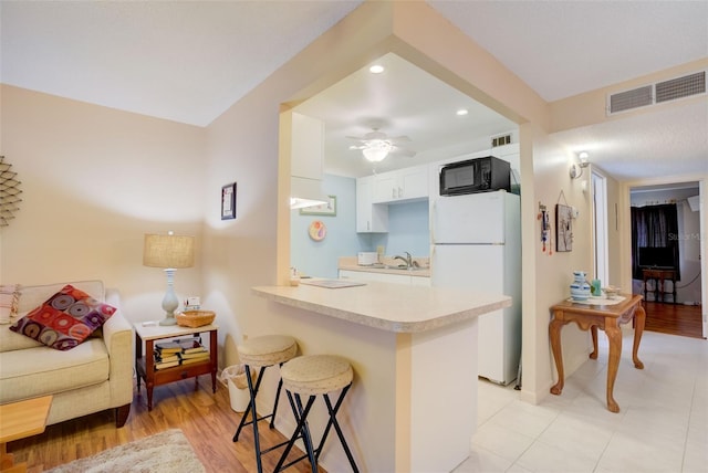 kitchen with ceiling fan, white refrigerator, kitchen peninsula, a breakfast bar area, and white cabinets