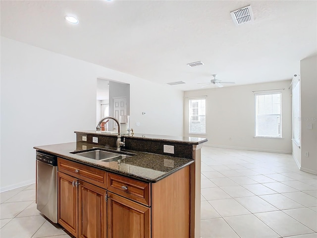 kitchen with stainless steel dishwasher, ceiling fan, sink, a center island with sink, and dark stone countertops