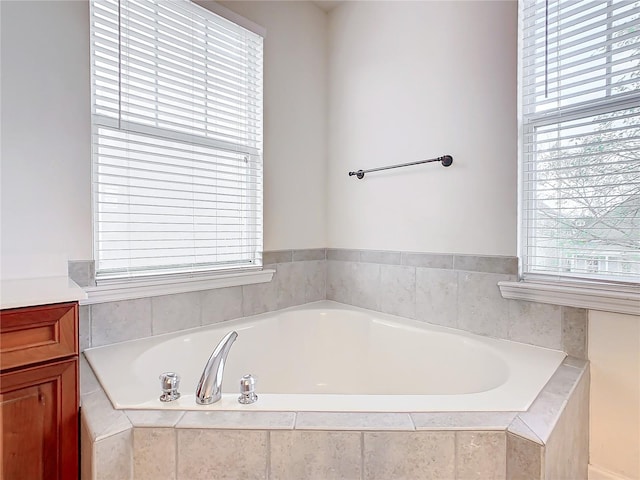 bathroom featuring plenty of natural light, vanity, and a relaxing tiled tub