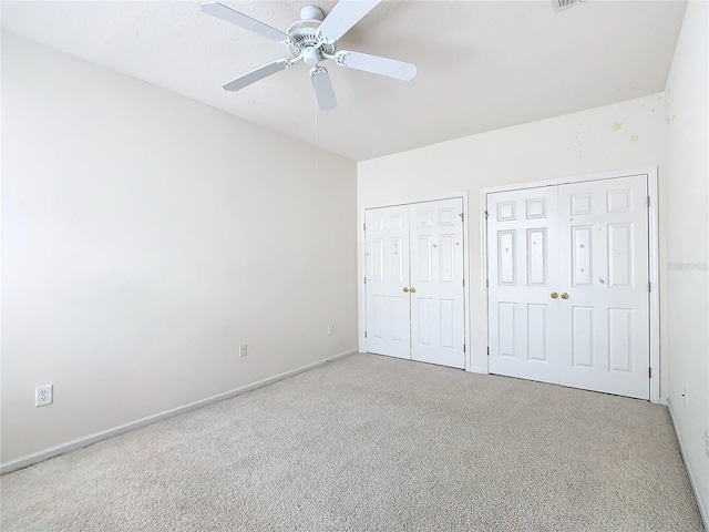 unfurnished bedroom featuring carpet floors, ceiling fan, and multiple closets