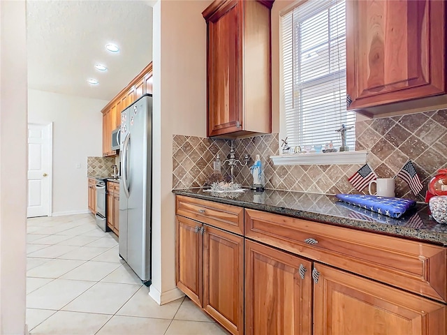 kitchen featuring decorative backsplash, light tile patterned floors, stainless steel appliances, and dark stone countertops