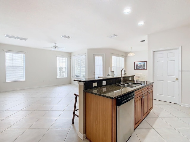 kitchen with sink, dishwasher, dark stone countertops, and an island with sink