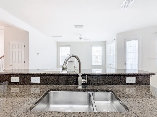 kitchen featuring ceiling fan, sink, and dark stone counters