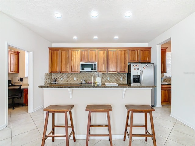 kitchen featuring a breakfast bar area, an island with sink, dark stone counters, and stainless steel appliances