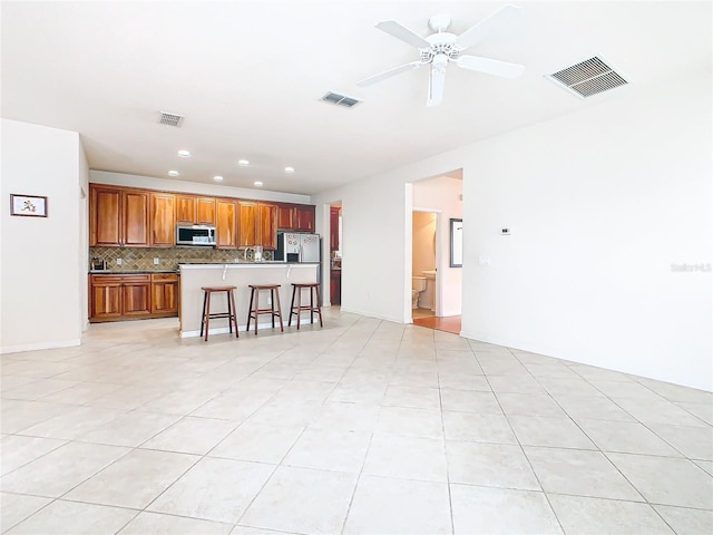 kitchen featuring ceiling fan, light tile patterned floors, a kitchen breakfast bar, backsplash, and a kitchen island