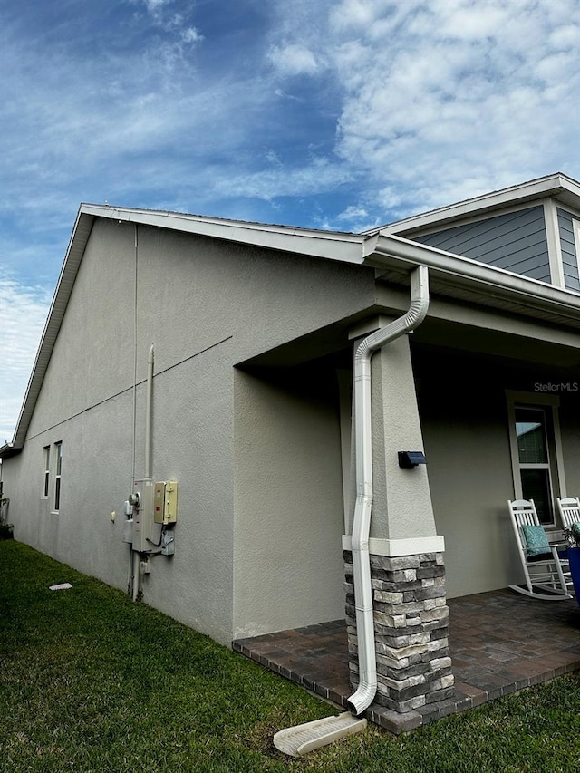 view of home's exterior featuring stucco siding, stone siding, a lawn, and covered porch