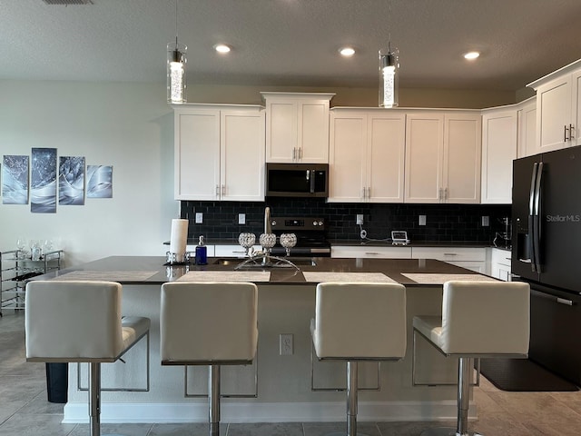 kitchen featuring range, white cabinets, a center island with sink, light tile patterned flooring, and black fridge