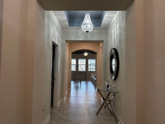 corridor with tile patterned floors, a raised ceiling, and a notable chandelier