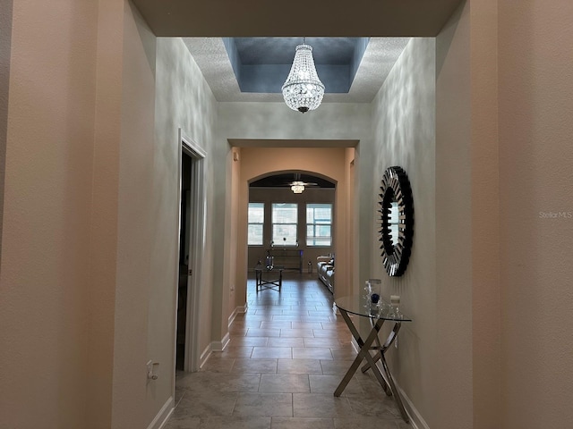 hallway featuring a tray ceiling, baseboards, and arched walkways