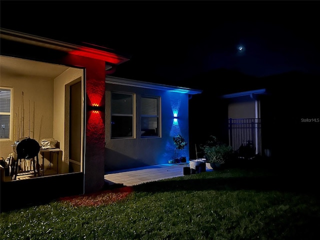 exterior entry at twilight featuring a lawn and stucco siding