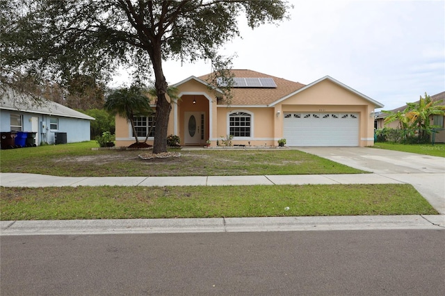 ranch-style home featuring central air condition unit, solar panels, a garage, and a front lawn