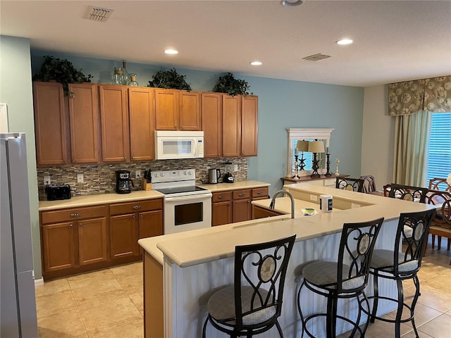 kitchen featuring a breakfast bar, an island with sink, sink, decorative backsplash, and white appliances