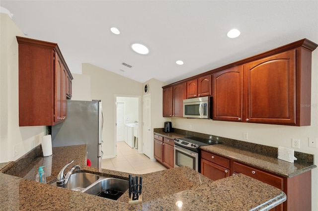 kitchen featuring stainless steel appliances, dark stone counters, vaulted ceiling, washing machine and dryer, and sink