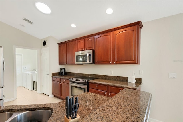 kitchen with stainless steel appliances, light tile flooring, dark stone counters, separate washer and dryer, and lofted ceiling