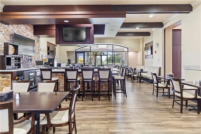 dining space featuring indoor bar, light hardwood / wood-style flooring, and beam ceiling