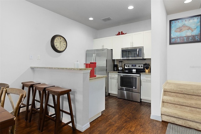 kitchen featuring a kitchen breakfast bar, appliances with stainless steel finishes, white cabinetry, backsplash, and dark hardwood / wood-style floors