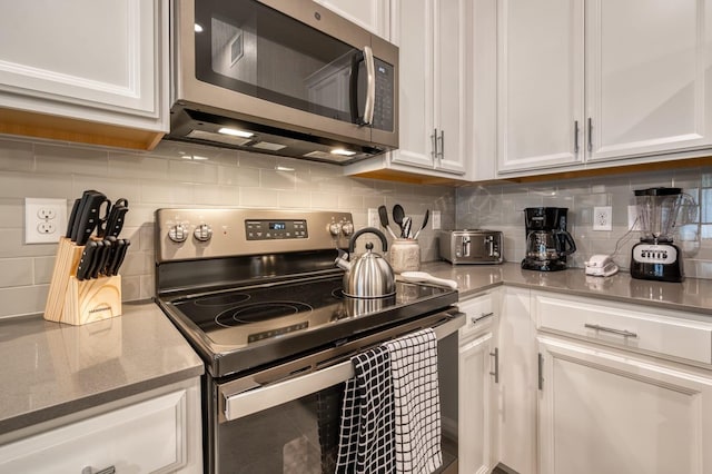 kitchen featuring dark stone countertops, white cabinets, backsplash, and stainless steel appliances